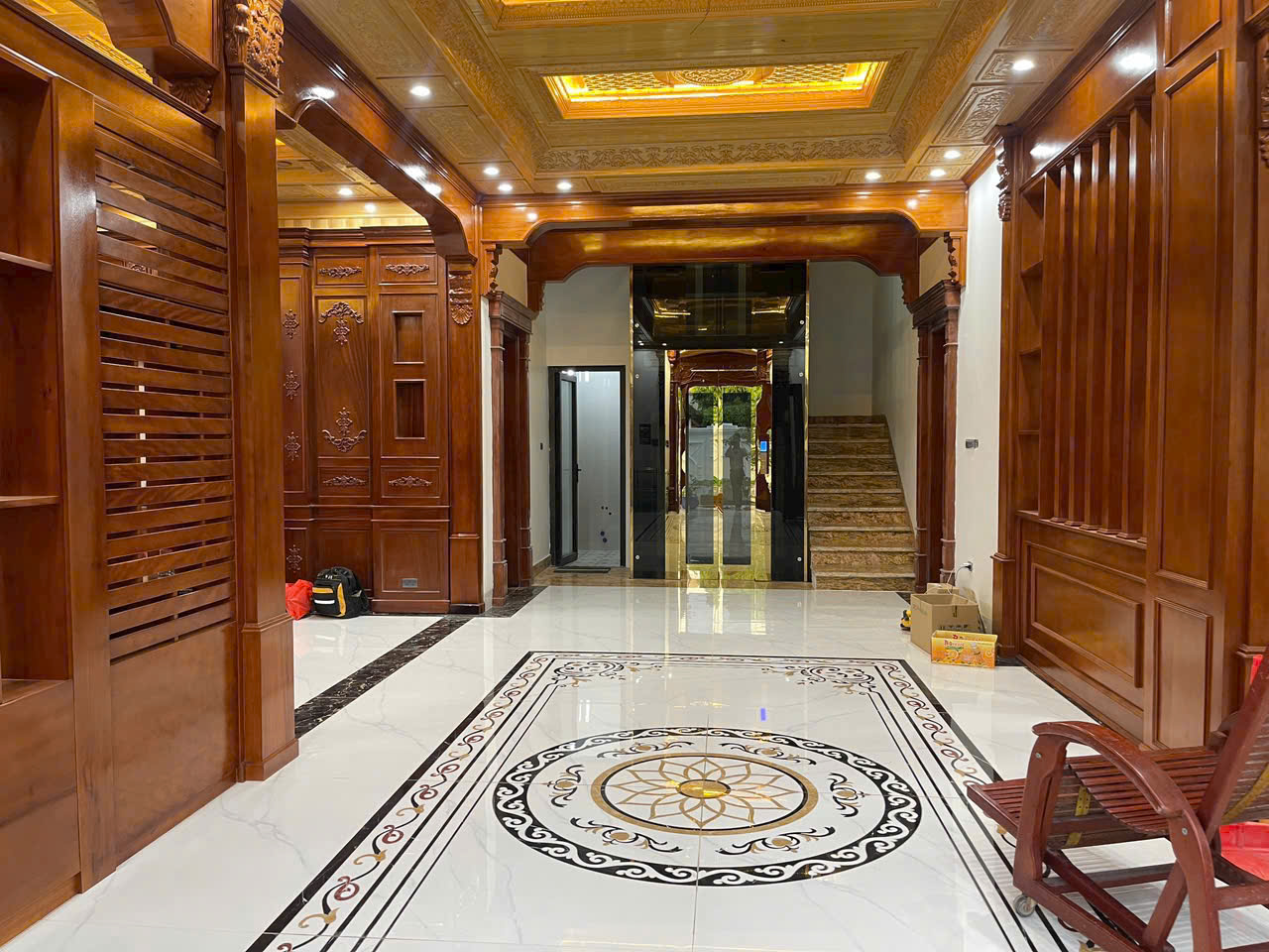 Nội thất sảnh nhà với vách gỗ tự nhiên chạm khắc, trần đèn led và nền gạch hoa văn cao cấp